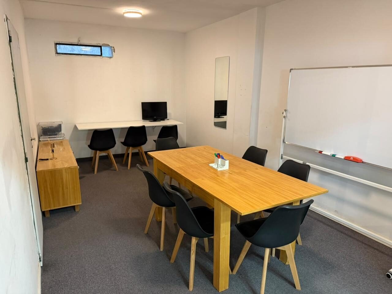 Sala de preproducción con mesa de madera, sillas negras y pizarra